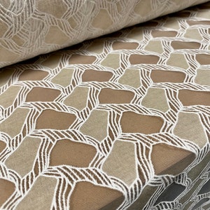 May include: White and beige geometric patterned lace fabric. The fabric has a mesh-like texture with a repeating pattern of overlapping shapes.