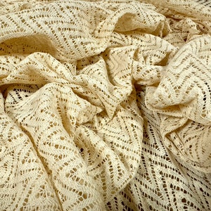 May include: Cream-coloured crochet fabric with a delicate, geometric pattern. The fabric is soft and lightweight, making it ideal for a variety of crafting projects.