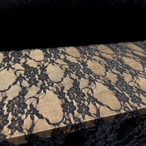 May include: Black lace fabric with a delicate floral pattern. The lace is sheer and has a soft, flowing texture.