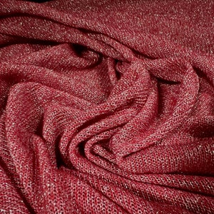 May include: Close-up of a red fabric with a sparkly, woven texture. The fabric is folded and draped, creating a soft, flowing look.