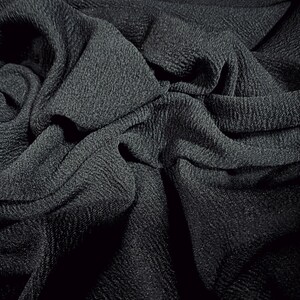 May include: Close-up of a black textured fabric with a crinkled and folded appearance.