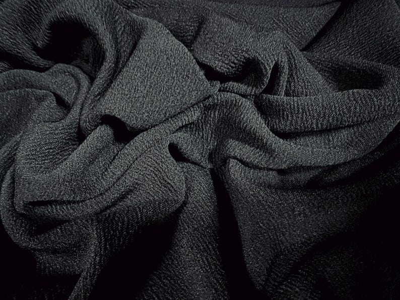 May include: Close-up of a black textured fabric with a crinkled and folded appearance.