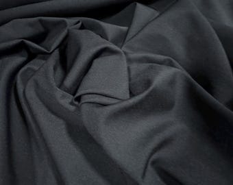 May include: Close-up of a dark gray fabric with soft folds and shadows. The material appears to be smooth and drapes naturally, creating a textured effect. The fabric's color is consistent throughout, with subtle variations in light and dark areas.