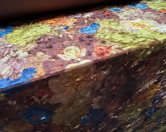 Könnte beinhalten: Nahaufnahme eines braunen Samtstoffes mit einem floralen Muster in Gold-, Grün-, Blau- und Rottönen.