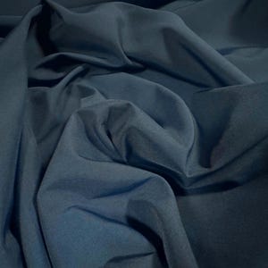 Pode incluir: Um close-up de um tecido azul escuro com uma textura lisa e sedosa. O tecido está dobrado e drapeado, mostrando sua natureza suave e fluida.