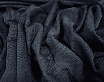 May include: Close-up of a dark gray ribbed fabric with a textured surface. The fabric is folded and draped, creating soft folds and curves.