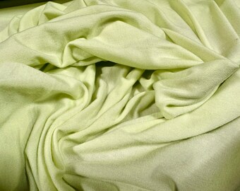 May include: A close-up of a light green fabric with a soft, smooth texture. The fabric is folded and draped, creating a sense of movement and flow.