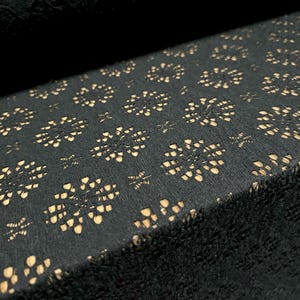 May include: Black fabric with a delicate, repeating pattern of small, cut-out floral shapes. The fabric has a subtle sheen and a soft texture.