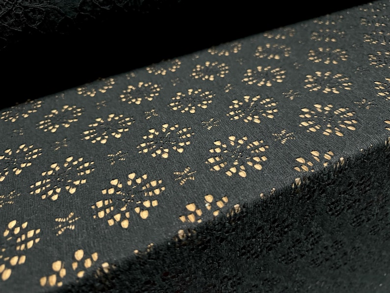 May include: Black fabric with a delicate, repeating pattern of small, cut-out floral shapes. The fabric has a subtle sheen and a soft texture.