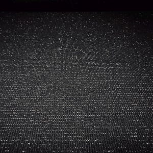 May include: A close-up view of a black fabric with a subtle, textured weave. The fabric is densely covered with tiny, sparkling silver flecks, creating a shimmering effect. The overall appearance is dark and elegant.