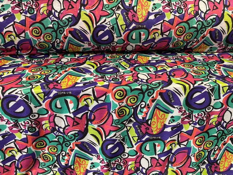May include: White fabric with a colorful, abstract, graffiti-style print. The print features swirls, geometric shapes, and the repeated text "Hot Mess".