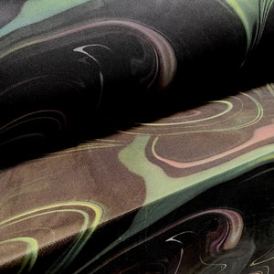 May include: Close-up of a black fabric with a swirling green, yellow, and pink marbled pattern.