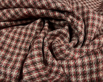 May include: Close-up of a houndstooth fabric with a repeating pattern in shades of brown, red, and cream. The fabric is tightly woven and has a textured appearance, with visible folds and creases.