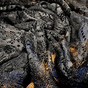 May include: Black lace fabric with a delicate floral pattern. The fabric is soft and flowing, with a slightly textured surface.