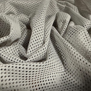 以下が含まれることがあります： 小さな穴が均等に配置されたパターンを持つ、明るい灰色のメッシュ生地のクローズアップ。生地はドレープされ、折りたたまれ、影とテクスチャを作り出しています。この素材は軽量で通気性があり、衣類などに適しているようです。