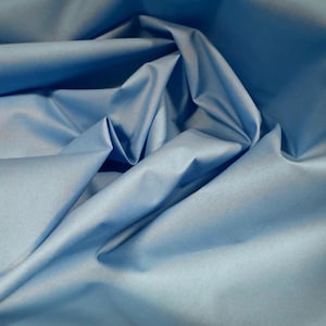 May include: A close-up of a light blue fabric with a smooth, silky texture. The fabric is folded and draped, creating soft folds and curves.