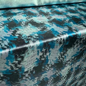 May include: A close-up of a blue and white patterned fabric with a satin finish. The fabric has a subtle sheen and a modern abstract design.