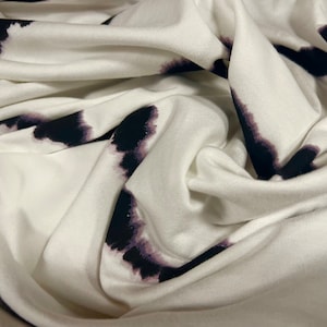 May include: White fabric with a black and purple tie-dye pattern. The fabric is soft and has a smooth texture.