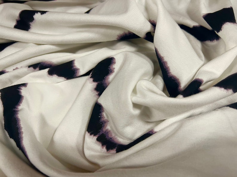 May include: White fabric with a black and purple tie-dye pattern. The fabric is soft and has a smooth texture.