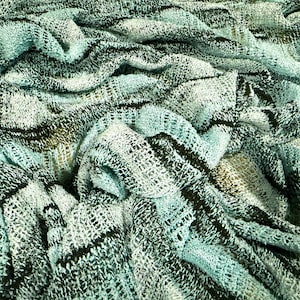 Könnte beinhalten: Ein gestrickter Stoff mit einer lockeren, offen gewebten Textur in einer Farbpalette aus hellem Minzgrün, dunklem Anthrazit und Schwarz. Das Material zeigt eine Reihe horizontaler, wellenförmiger Streifen, die ein geschichtetes Aussehen erzeugen.