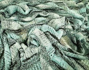May include: A knitted fabric featuring a loose, open-weave texture with a colour palette of light mint green, dark charcoal, and black. The material displays a series of horizontal, wavy stripes that create a layered, dimensional appearance.
