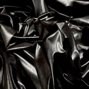 Peut inclure: Gros plan sur un tissu noir avec une surface brillante et réfléchissante. Le tissu est fortement drapé, créant des ombres et des reflets profonds. Le matériau semble lisse et luxueux, avec un éclat subtil.