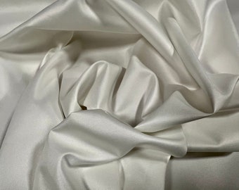 May include: White satin fabric with a smooth, silky texture. The fabric is folded and draped, creating soft folds and curves.