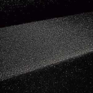 May include: Close-up of a black fabric with a textured, ribbed surface. The fabric has a subtle sparkle, catching the light and creating a shimmering effect. The material is folded, showing depth and dimension.