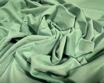 May include: A close-up of a soft, green fabric with a smooth texture. The fabric is folded and draped, showing its draping qualities.