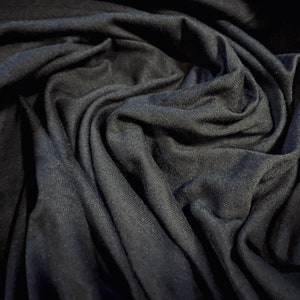 May include: Close-up of a dark gray fabric with a soft, wrinkled texture. The fabric is draped and folded, creating a sense of depth and dimension.