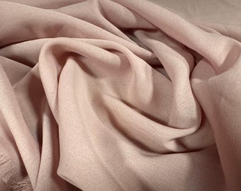 Könnte beinhalten: Nahaufnahme eines weichen, fließenden Stoffes in einem gedämpften Rosaton. Das Material ist drapiert und gerafft, wodurch sanfte Falten und Schatten entstehen. Die Textur erscheint leicht strukturiert, mit einem dezenten Glanz.