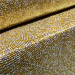 May include: Gold fabric with a white and red patterned design. The fabric has a metallic sheen and a textured surface.