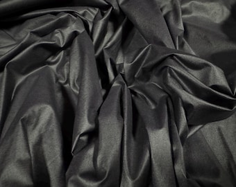May include: A close-up of a dark gray fabric with a smooth, silky texture. The fabric is draped and folded, creating soft, flowing lines.