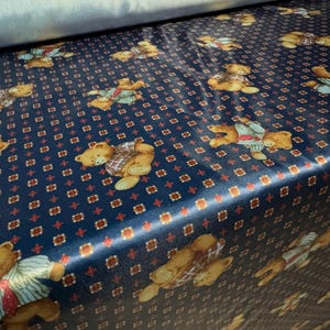 May include: Blue fabric with a repeating pattern of brown teddy bears wearing blue and white shirts. The fabric has a small red and white diamond pattern.