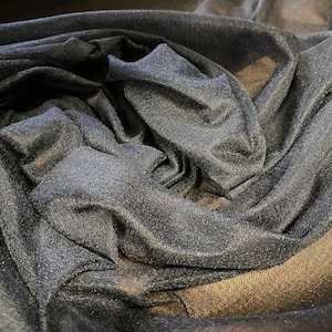 May include: Black sheer fabric with a sparkly finish. The fabric is draped and folded, showing its texture and sheen.