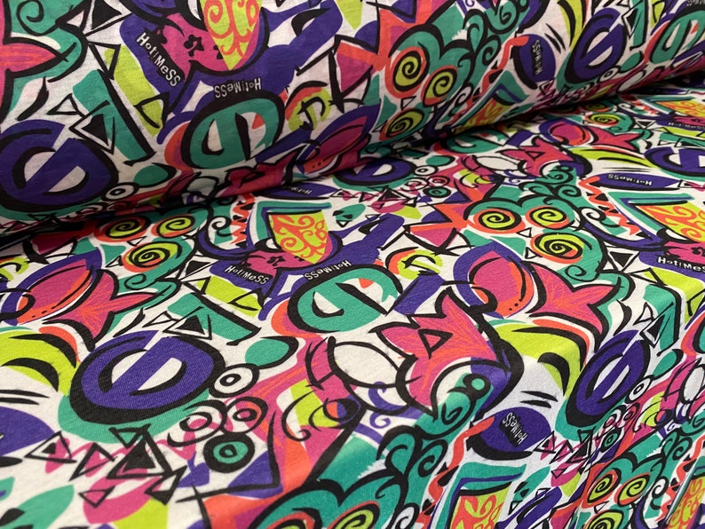 May include: White fabric with a colorful, abstract print featuring geometric shapes, swirls, and the words "Hot Mess" and "Switch".