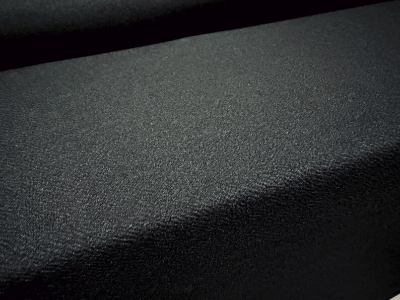 May include: Close-up of a black textured fabric. The fabric has a subtle, pebbled texture.