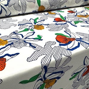 May include: White fabric with a floral pattern. The flowers are outlined in black and blue, with orange and red accents. The background is white with thin blue stripes.