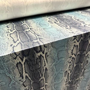 May include: Close-up of a fabric with a blue and grey snakeskin pattern. The fabric is folded over, showing the underside of the material.