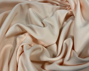May include: A close-up of a soft, peach-coloured fabric with a smooth texture. The fabric is draped and folded, creating a luxurious and elegant look.
