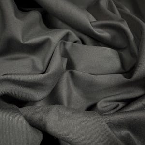 Puede incluir: Primer plano de una tela gris oscuro con una textura acanalada sutil. La tela está doblada y drapeada, mostrando su superficie suave y lisa.