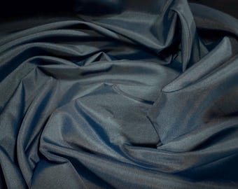 May include: A close-up of a dark blue fabric with a smooth, silky texture. The fabric is draped and folded, creating soft, flowing lines.