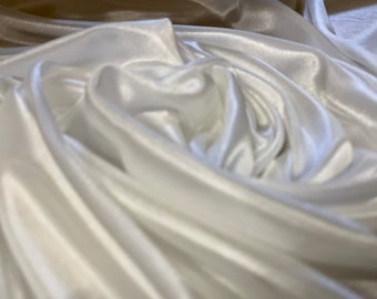May include: Close-up of white satin fabric with soft folds and a lustrous sheen. The fabric appears to be draped, creating a sense of depth and texture. The folds catch the light, highlighting the smooth surface.
