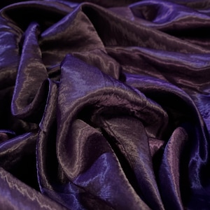 May include: Close-up of a deep purple satin fabric with a smooth, silky texture. The fabric is draped and folded, creating soft, flowing lines.