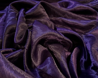May include: Close-up of a deep purple satin fabric with a smooth, silky texture. The fabric is draped and folded, creating soft, flowing lines.
