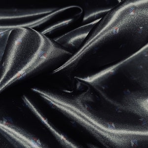 May include: Black satin fabric with a subtle pattern of small, colorful triangles.