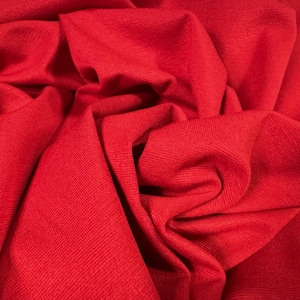 Pode incluir: Close-up de um tecido vermelho com superfície texturizada. O tecido está dobrado e drapeado, criando um visual suave e convidativo.