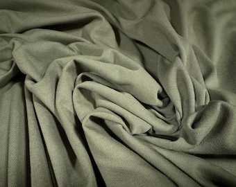 May include: Close-up of a soft, green fabric with a textured surface. The fabric is folded and draped, creating a series of folds and creases.
