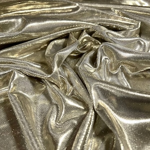 May include: Close-up of a gold metallic fabric with a textured surface. The fabric is wrinkled and has a shiny, reflective finish.
