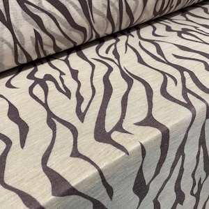 May include: Close-up of a beige fabric with a black zebra print pattern. The fabric is folded in half, showing the pattern on both sides.